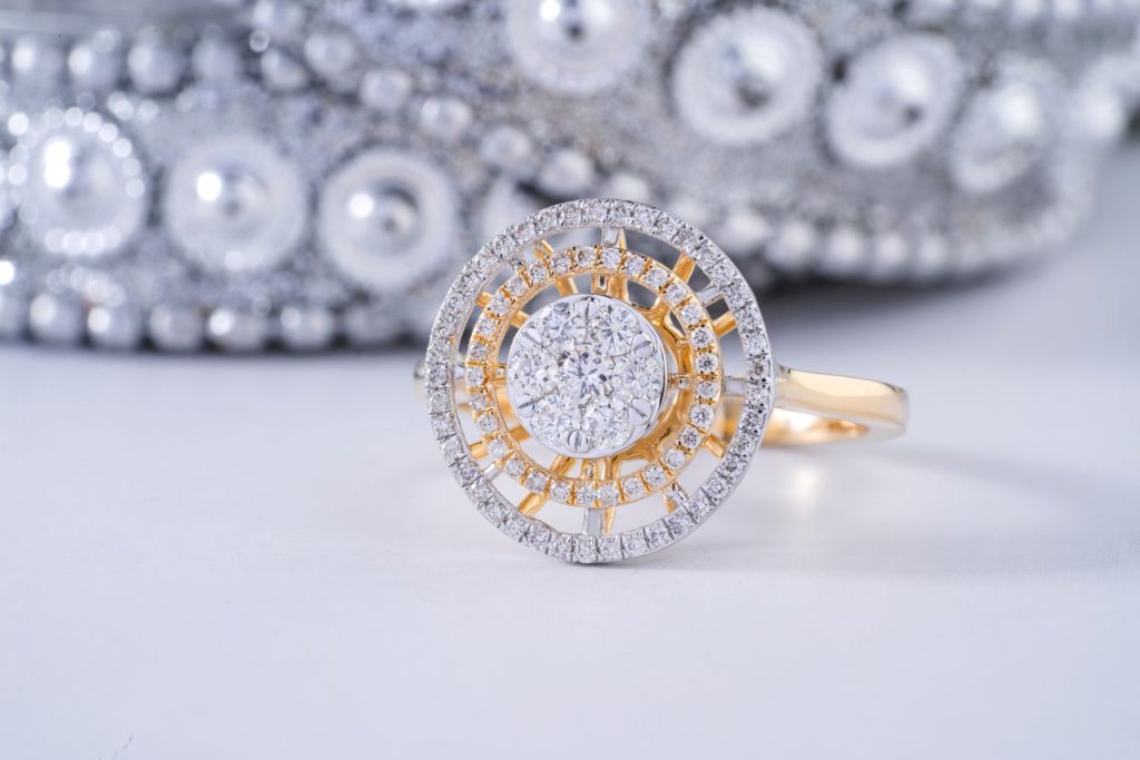 Close-up of an elegant diamond ring with intricate design on a reflective surface.